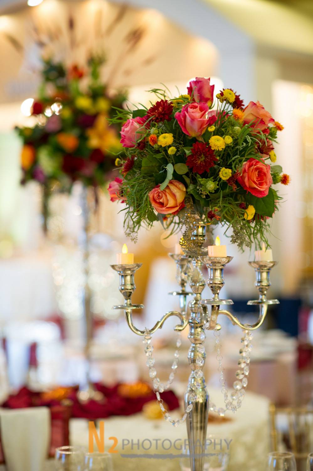 Luxurious floral arrangement with vibrant roses and chrysanthemums atop a silver candelabra centerpiece, highlighting Alegria Gardens’ precision in event decor. Luxurious floral arrangement with vibrant roses and chrysanthemums atop a silver candelabra centerpiece, highlighting Alegria Gardens’ precision in event decor.