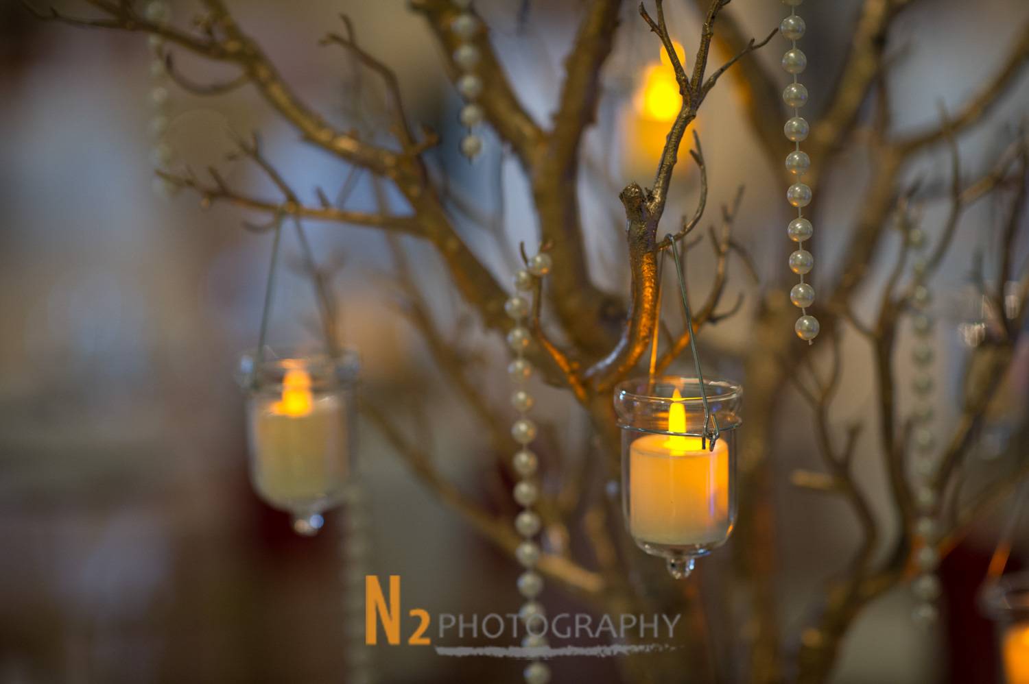 Close-up of hanging candle decorations and pearl strands on a rustic branch centerpiece, reflecting the refined ambiance created by Alegria Gardens. Close-up of hanging candle decorations and pearl strands on a rustic branch centerpiece, reflecting the refined ambiance created by Alegria Gardens.